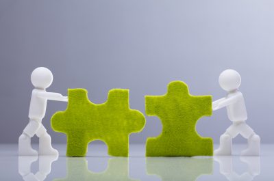 Two Miniature Human Figures Solving Green Jigsaw Puzzles