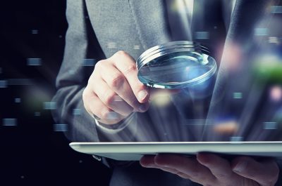 Businessman examines a tablet with a magnifying glass. Concept of internet security